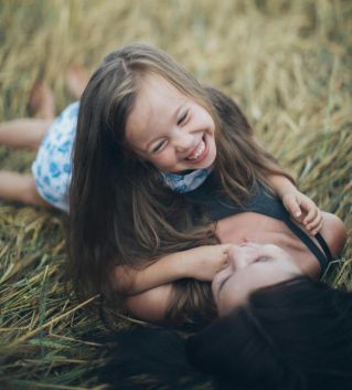 A joyful mother and daughter sharing a playful moment in a sunlit summer field.