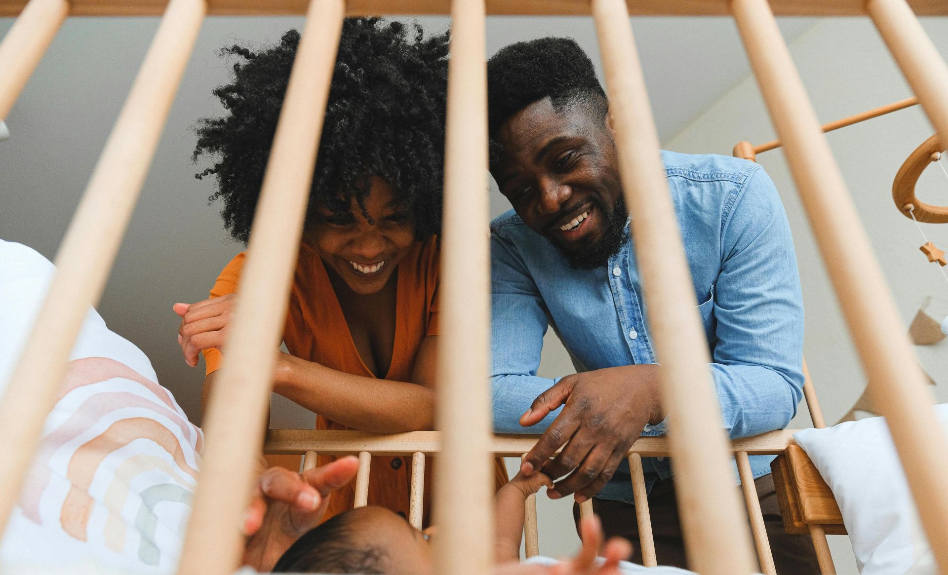 Joyful parents playing with their baby in a wooden crib.