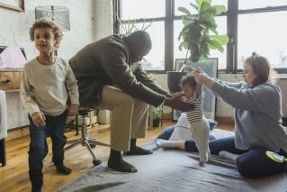 Multiracial family playing with children in casual outfit on textile on floor in light room near windows