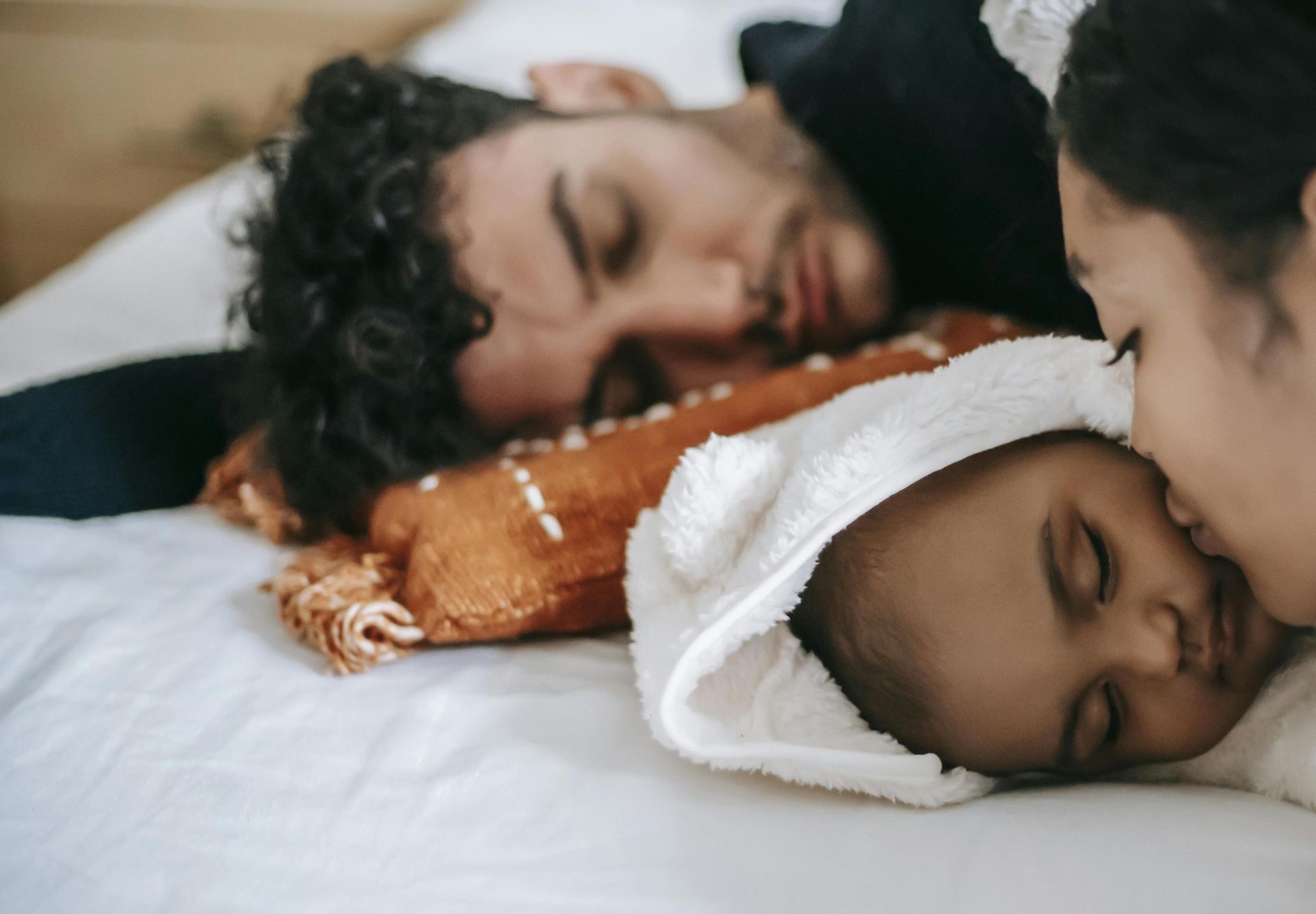 A peaceful family moment with parents and baby napping together in a cozy bedroom setting.